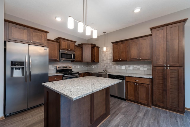 kitchen with sink, light stone counters, a kitchen island, pendant lighting, and stainless steel appliances