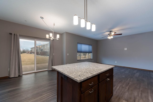 kitchen featuring dark wood-type flooring, a kitchen island, ceiling fan with notable chandelier, and hanging light fixtures