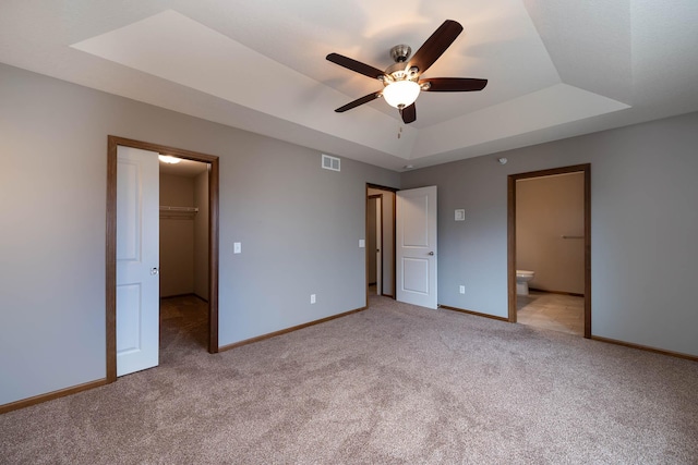 unfurnished bedroom with a spacious closet, light colored carpet, ceiling fan, a tray ceiling, and a closet