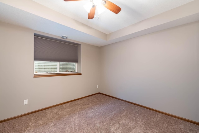 carpeted empty room with ceiling fan and a tray ceiling