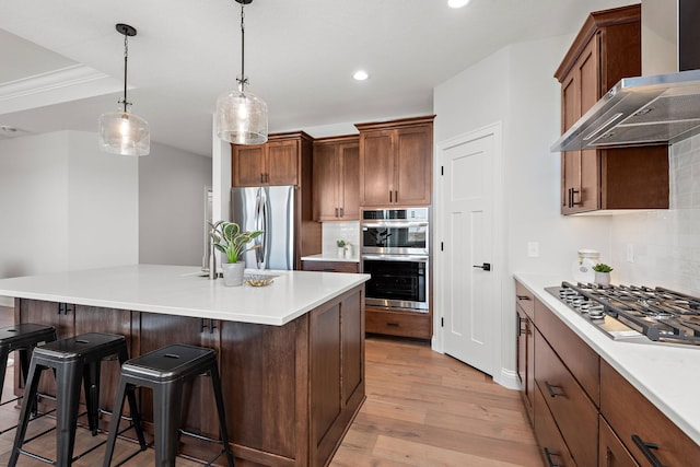 kitchen with wall chimney range hood, hanging light fixtures, backsplash, stainless steel appliances, and light hardwood / wood-style floors