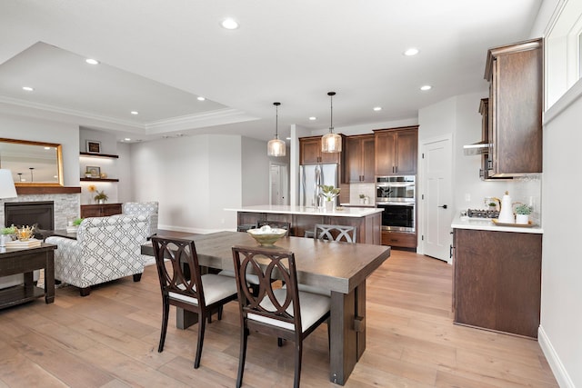 dining room featuring a raised ceiling, crown molding, a stone fireplace, and light hardwood / wood-style flooring