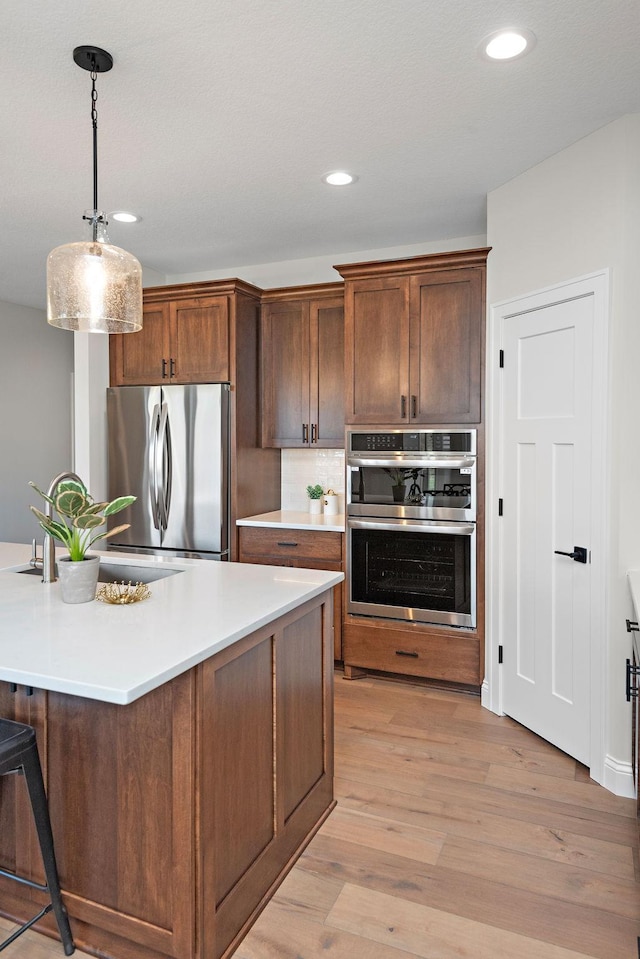 kitchen featuring hanging light fixtures, appliances with stainless steel finishes, sink, and light hardwood / wood-style floors