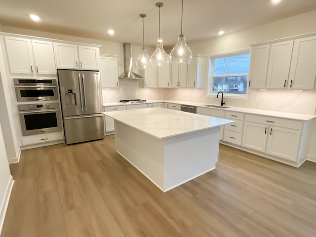 kitchen featuring stainless steel appliances, wall chimney range hood, white cabinets, and decorative light fixtures