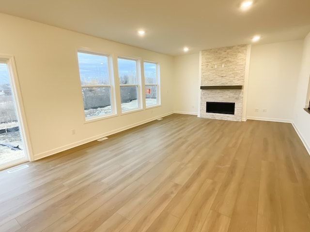 unfurnished living room featuring a stone fireplace and light wood-type flooring