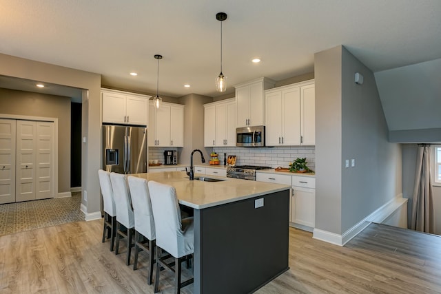 kitchen featuring sink, white cabinetry, hanging light fixtures, stainless steel appliances, and a center island with sink