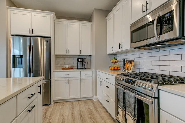 kitchen with tasteful backsplash, white cabinetry, stainless steel appliances, light stone countertops, and light wood-type flooring