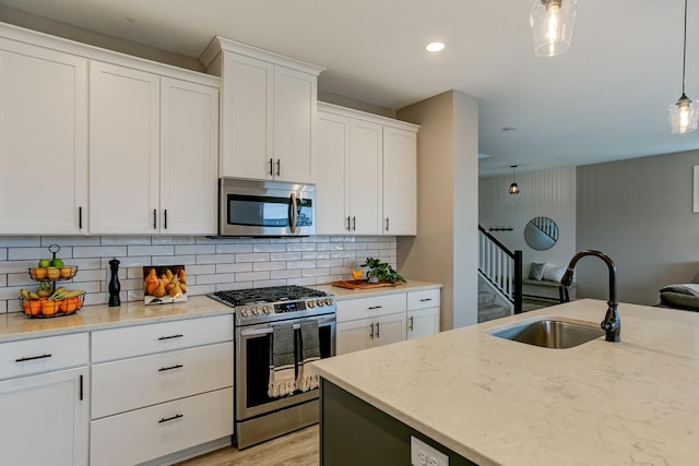 kitchen with sink, appliances with stainless steel finishes, pendant lighting, light stone countertops, and white cabinets