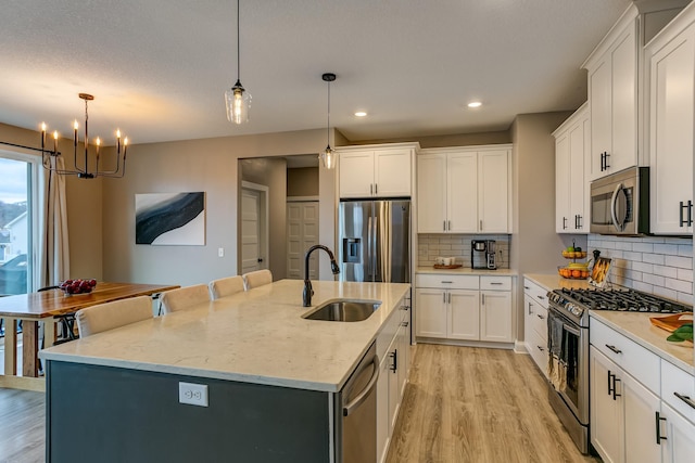 kitchen featuring sink, white cabinetry, stainless steel appliances, an island with sink, and decorative light fixtures