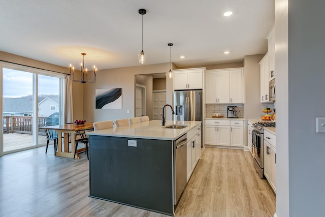 kitchen featuring a kitchen island with sink, hanging light fixtures, white cabinetry, and appliances with stainless steel finishes