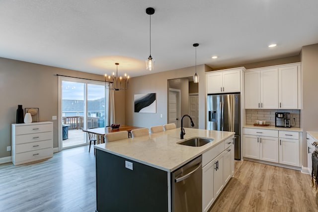 kitchen with sink, white cabinetry, stainless steel appliances, light stone counters, and an island with sink