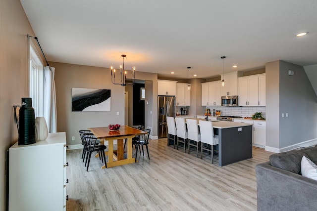 kitchen featuring appliances with stainless steel finishes, decorative light fixtures, white cabinetry, a kitchen breakfast bar, and a kitchen island with sink