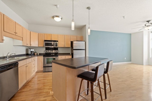 kitchen with sink, appliances with stainless steel finishes, hanging light fixtures, a center island, and light brown cabinets