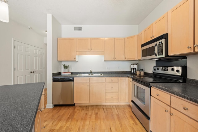 kitchen with sink, stainless steel appliances, light hardwood / wood-style floors, a textured ceiling, and light brown cabinetry