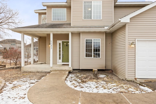 snow covered property entrance with a porch and a garage