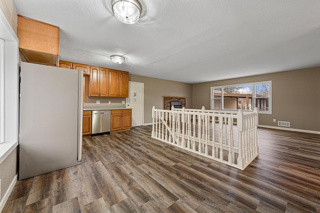 kitchen with a brick fireplace, dark hardwood / wood-style floors, a textured ceiling, and appliances with stainless steel finishes