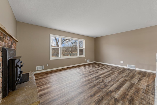 unfurnished living room with hardwood / wood-style flooring, a brick fireplace, and a textured ceiling