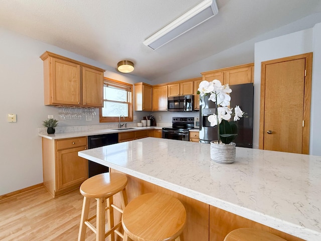 kitchen featuring light wood finished floors, a sink, stainless steel appliances, vaulted ceiling, and a kitchen bar