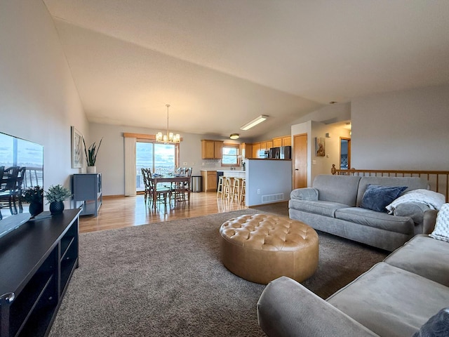 living room featuring visible vents, light colored carpet, light wood-type flooring, lofted ceiling, and a notable chandelier