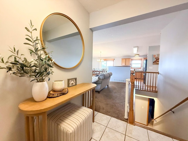 hall with visible vents, baseboards, light colored carpet, light tile patterned floors, and an inviting chandelier