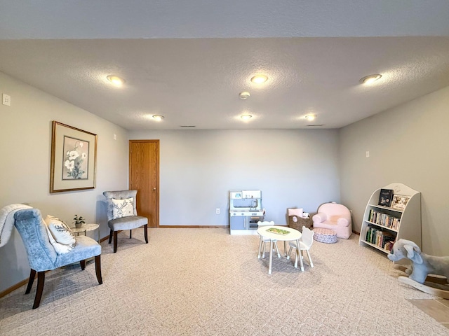 recreation room with light colored carpet, baseboards, and a textured ceiling