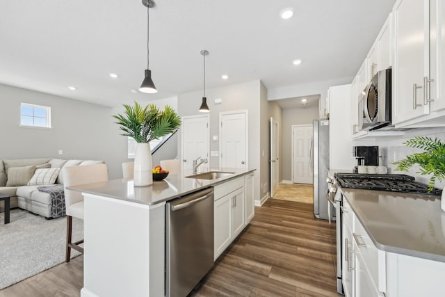 kitchen with sink, white cabinetry, hanging light fixtures, stainless steel appliances, and a kitchen island with sink