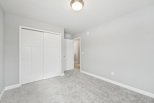 unfurnished bedroom featuring light colored carpet, a textured ceiling, and a closet