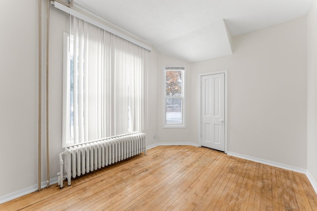 spare room with hardwood / wood-style flooring, vaulted ceiling, and radiator heating unit