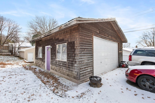 snow covered property featuring a garage and an outbuilding