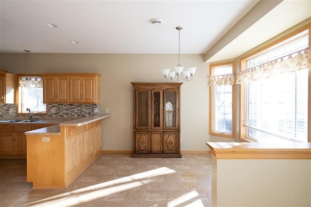 kitchen with decorative light fixtures, sink, backsplash, kitchen peninsula, and an inviting chandelier