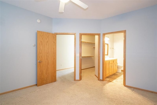 unfurnished bedroom featuring ensuite bathroom, a spacious closet, light colored carpet, a closet, and ceiling fan