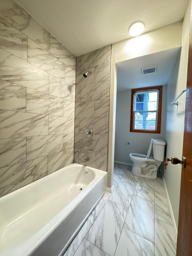 bathroom featuring tiled shower / bath, a textured ceiling, and toilet