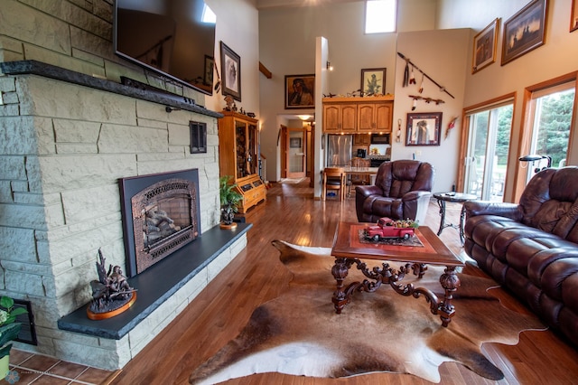 living room featuring a high ceiling, a stone fireplace, and dark hardwood / wood-style floors