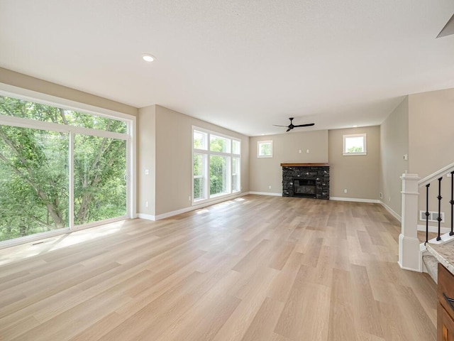 unfurnished living room with a stone fireplace, plenty of natural light, light hardwood / wood-style floors, and ceiling fan