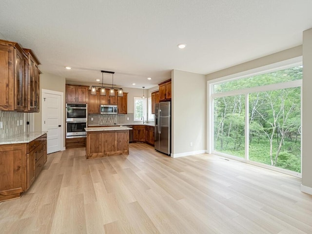 kitchen featuring tasteful backsplash, decorative light fixtures, a center island, light wood-type flooring, and appliances with stainless steel finishes