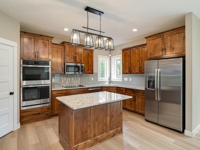 kitchen featuring decorative light fixtures, sink, a center island, light stone counters, and stainless steel appliances