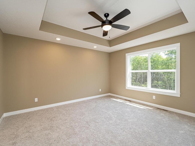 spare room with ceiling fan, a raised ceiling, and carpet