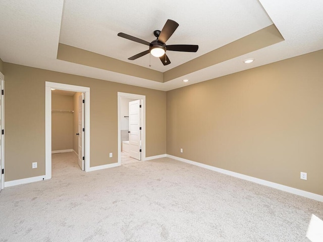 unfurnished bedroom with ceiling fan, ensuite bathroom, a tray ceiling, a walk in closet, and a closet