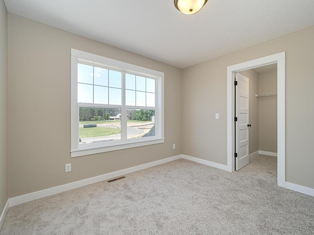 unfurnished bedroom with light colored carpet, a spacious closet, and a closet