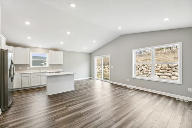 kitchen with stainless steel refrigerator with ice dispenser, lofted ceiling, a center island, and white cabinets