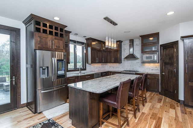 kitchen featuring sink, hanging light fixtures, stainless steel appliances, a center island, and wall chimney exhaust hood