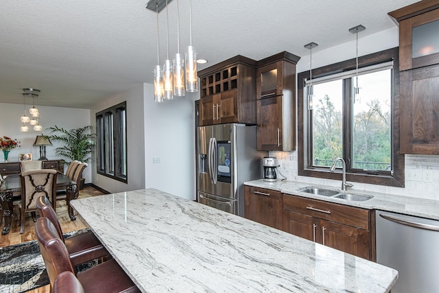 kitchen with sink, light stone counters, a textured ceiling, appliances with stainless steel finishes, and backsplash