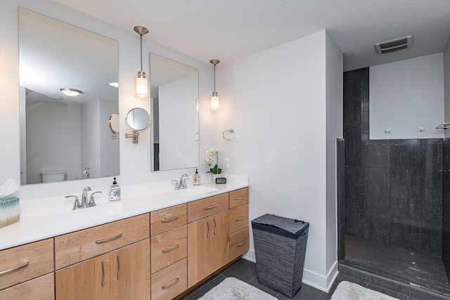 bathroom featuring vanity, a textured ceiling, toilet, and a tile shower