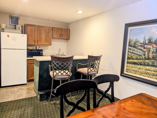 kitchen featuring black microwave, a sink, visible vents, light countertops, and freestanding refrigerator