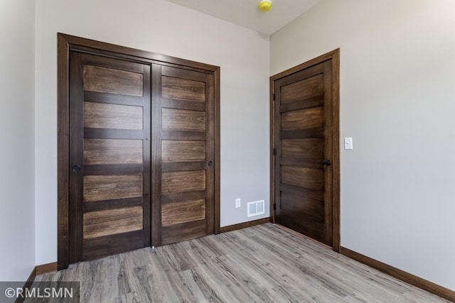 unfurnished bedroom with visible vents, light wood-style flooring, and baseboards