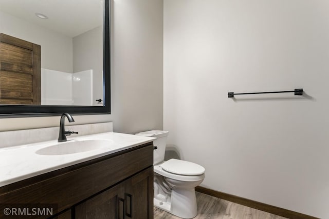 bathroom featuring baseboards, toilet, wood finished floors, and vanity