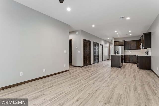 kitchen featuring stainless steel fridge with ice dispenser, a kitchen island with sink, light countertops, dark brown cabinetry, and light wood-type flooring