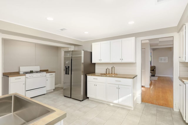 kitchen with stainless steel refrigerator with ice dispenser, white gas range, and white cabinets