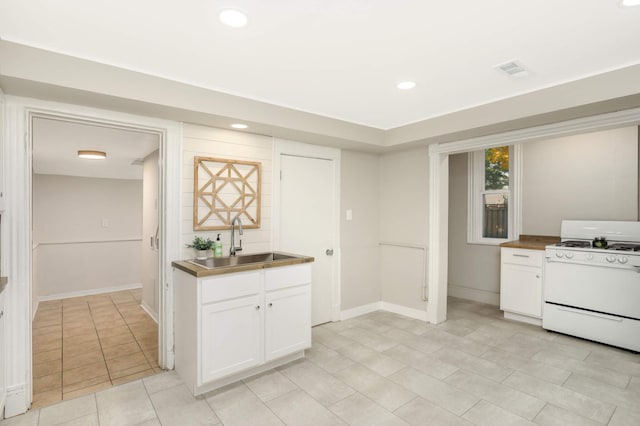 kitchen featuring light tile patterned floors, sink, white range with gas stovetop, and white cabinets