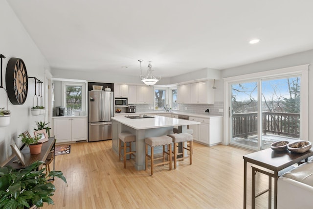 kitchen with a kitchen island, appliances with stainless steel finishes, pendant lighting, white cabinets, and light hardwood / wood-style flooring